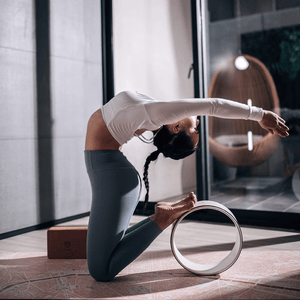 Woman performing backbend yoga pose on Yogasana Daylight Paris map mat using yoga wheel.