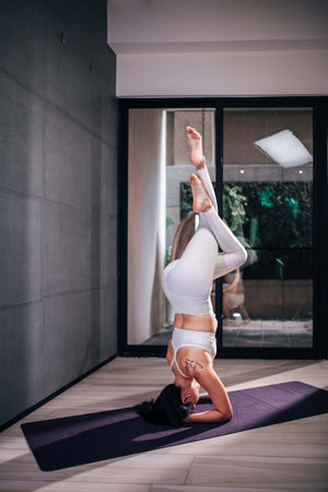 Woman in white activewear performing headstand on YOGASANA Glamorous Barcelona yoga mat under indoor lighting.