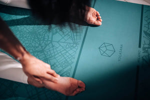 Close-up of YOGASANA logo and hand touching the Renaissance Milan green yoga mat, showing fine detail.