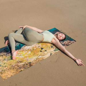 Model relaxing on Yogasana Landscape Collection Island Garden yoga towel at the beach, inspired by Tasmanian coastal landscape.