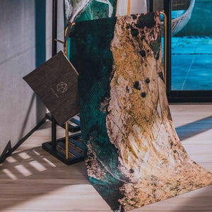 Close-up of Yogasana Landscape Collection Island Garden towel with ocean-inspired rocky cliff print, displayed in modern yoga studio.