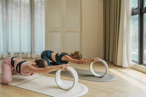 Models in extended stretch pose with yoga wheels on YOGASANA Lumiere Sundial 4mm Half-Round Natural Rubber Yoga Mats, capturing harmony and mindful motion.