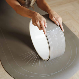 Woman stretching on yoga mat using Lumiere Sundial Yoga Wheel – Dune, showing the elegant silver sun pattern and minimalist design.