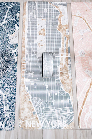 Yogasana Urban Collection yoga wheels and mats featuring city map designs of New York, Paris, and Barcelona in a minimalist indoor flat lay.