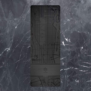 Flat lay of the Urban Sketch 4mm Natural Rubber Yoga Mat in Midnight New York design, featuring a city map pattern on a dark marble background.
