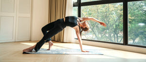 Woman practicing yoga in YOGASANA activewear on a natural rubber mat beside a sunlit window, expressing balance and comfort in motion