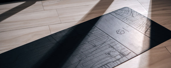 Yogasana premium yoga mat with minimalist urban design on wooden floor, featured in the Contact Us page banner.