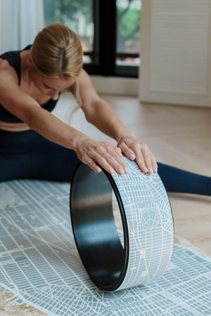 Woman stretching forward with Yogasana Urban Portrait Yoga Wheel featuring grey and white New York map print.