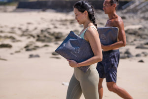 Woman carrying Yogasana yoga towel in a grey carry pouch while walking on the beach